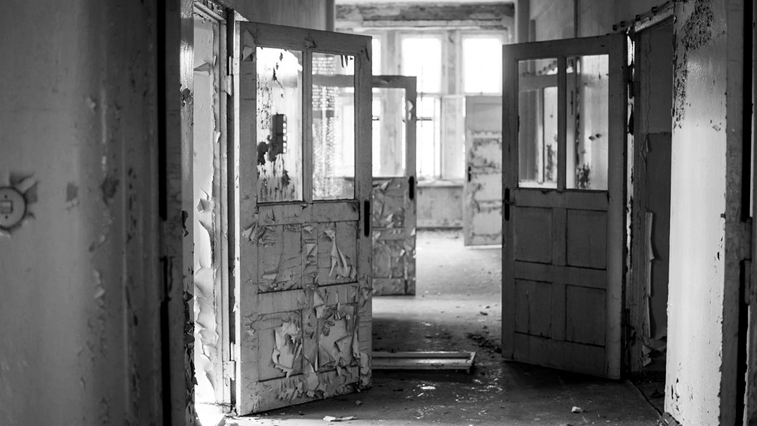 Photograph of a rundown hallway damaged, open doors.