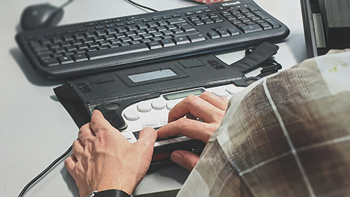 Someone using an assistive technology keyboard in front of a standard keyboard.